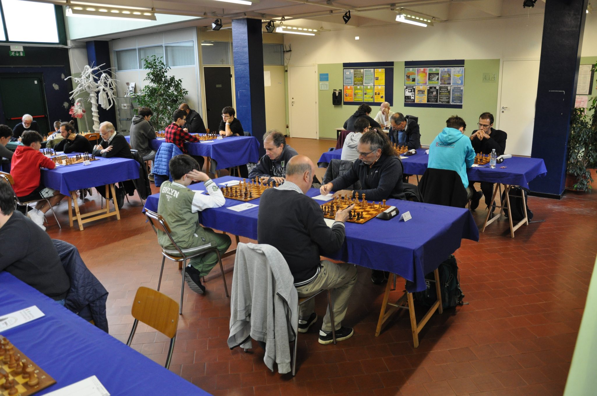A group of individuals participating in a chess tournament, seated at tables covered with blue tablecloths, focused on their games.