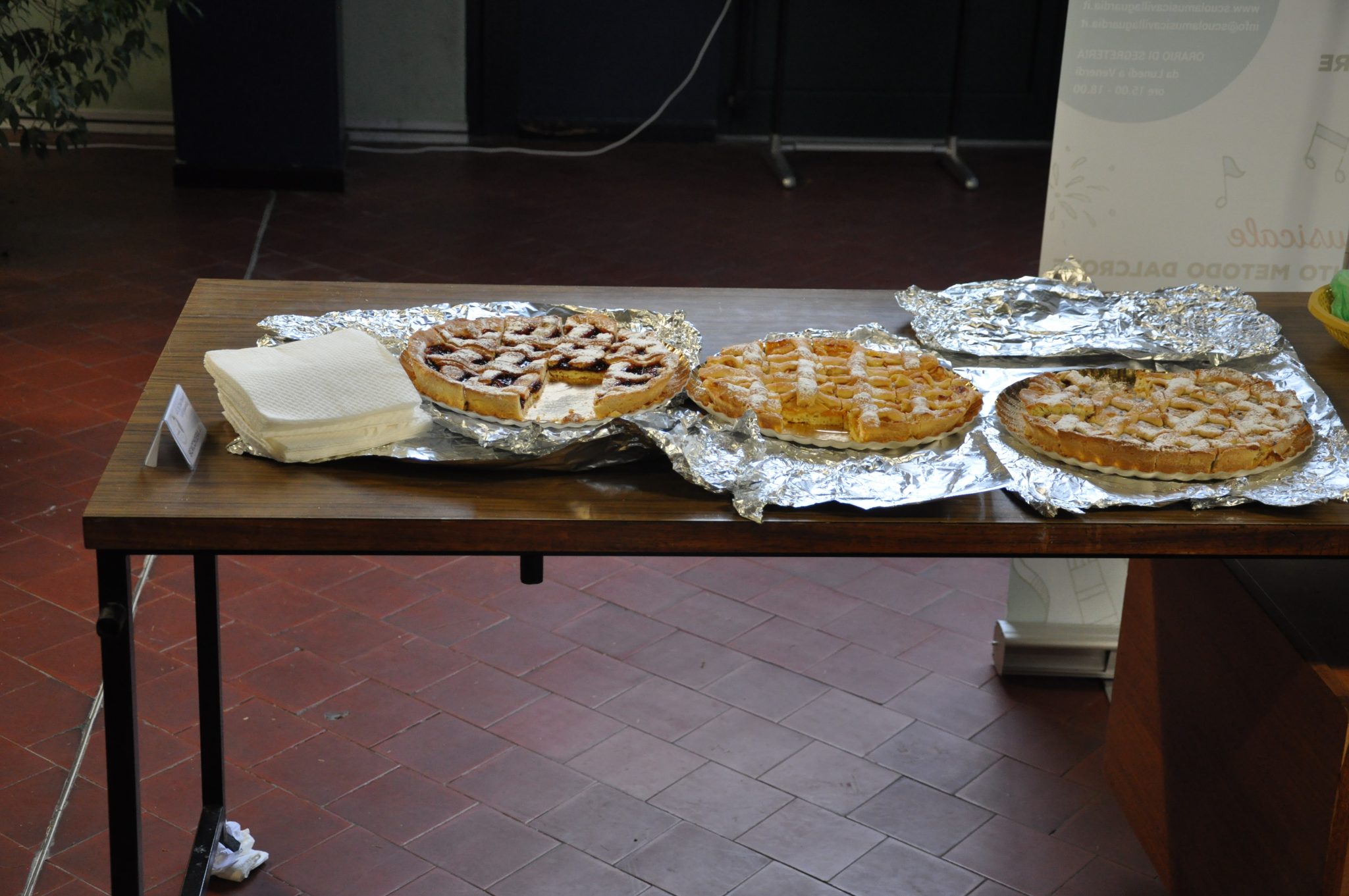 A wooden table displaying several baked goods, including round pies on aluminum foil. Three distinct pies are visible, showcasing different toppings and presentations.