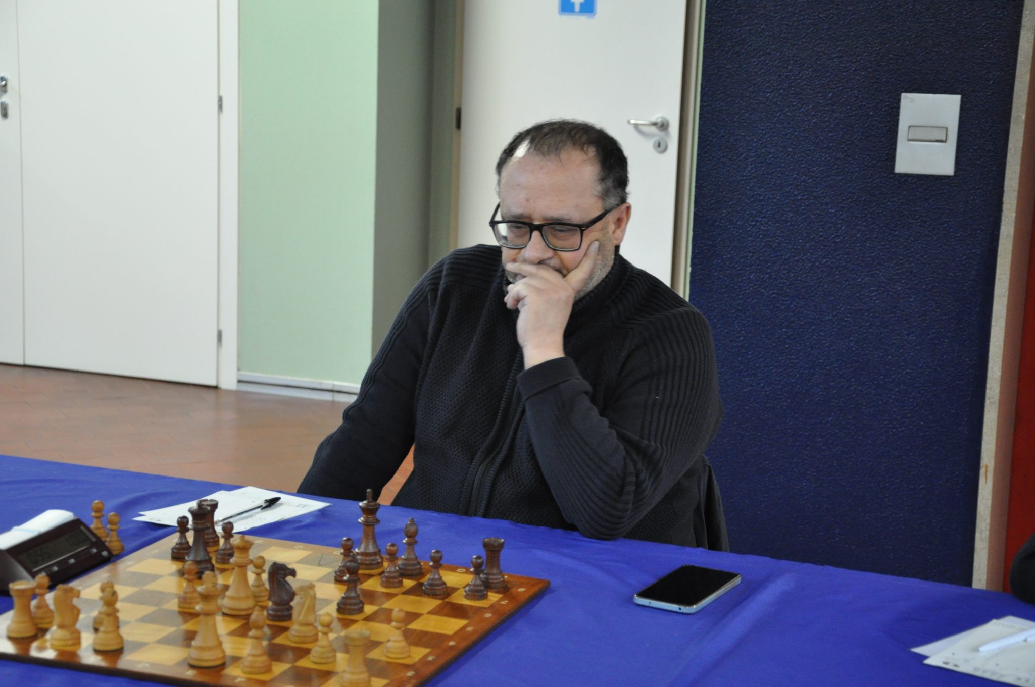 A person deep in thought while playing chess, with a chessboard in front and a smartphone nearby.