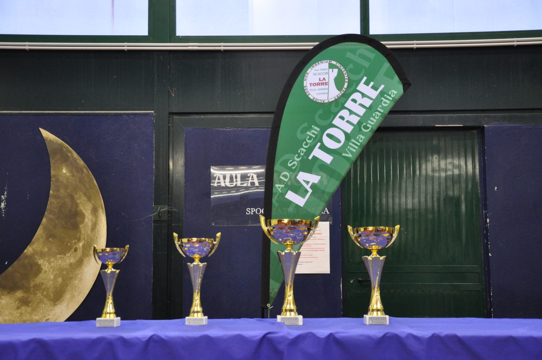 Four trophies displayed on a blue tablecloth beside a green banner with 'LA TORRE' written on it.