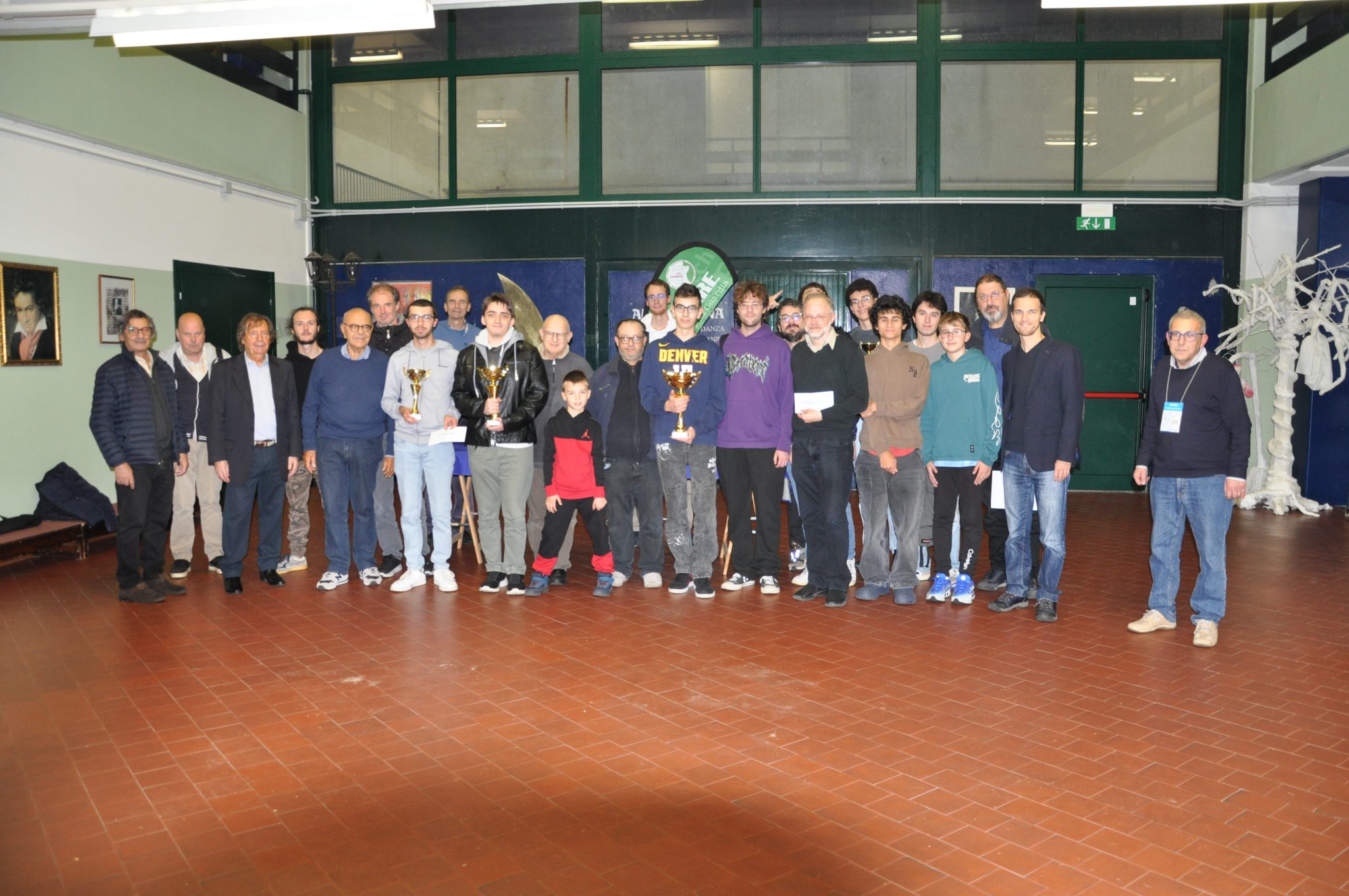 Group photo of participants and organizers at an event, posing together with trophies indoors.