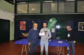 A young man receiving a trophy and a check from an older man during an award ceremony in a spacious indoor venue.