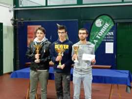 Three young winners holding trophies at an awards ceremony, with a green banner in the background.