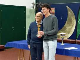 Two men posing together with a trophy in a room decorated with a moon backdrop.