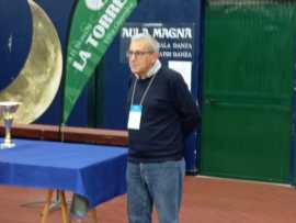 A man standing near a trophy on a table in a gymnasium, with a green banner in the background.