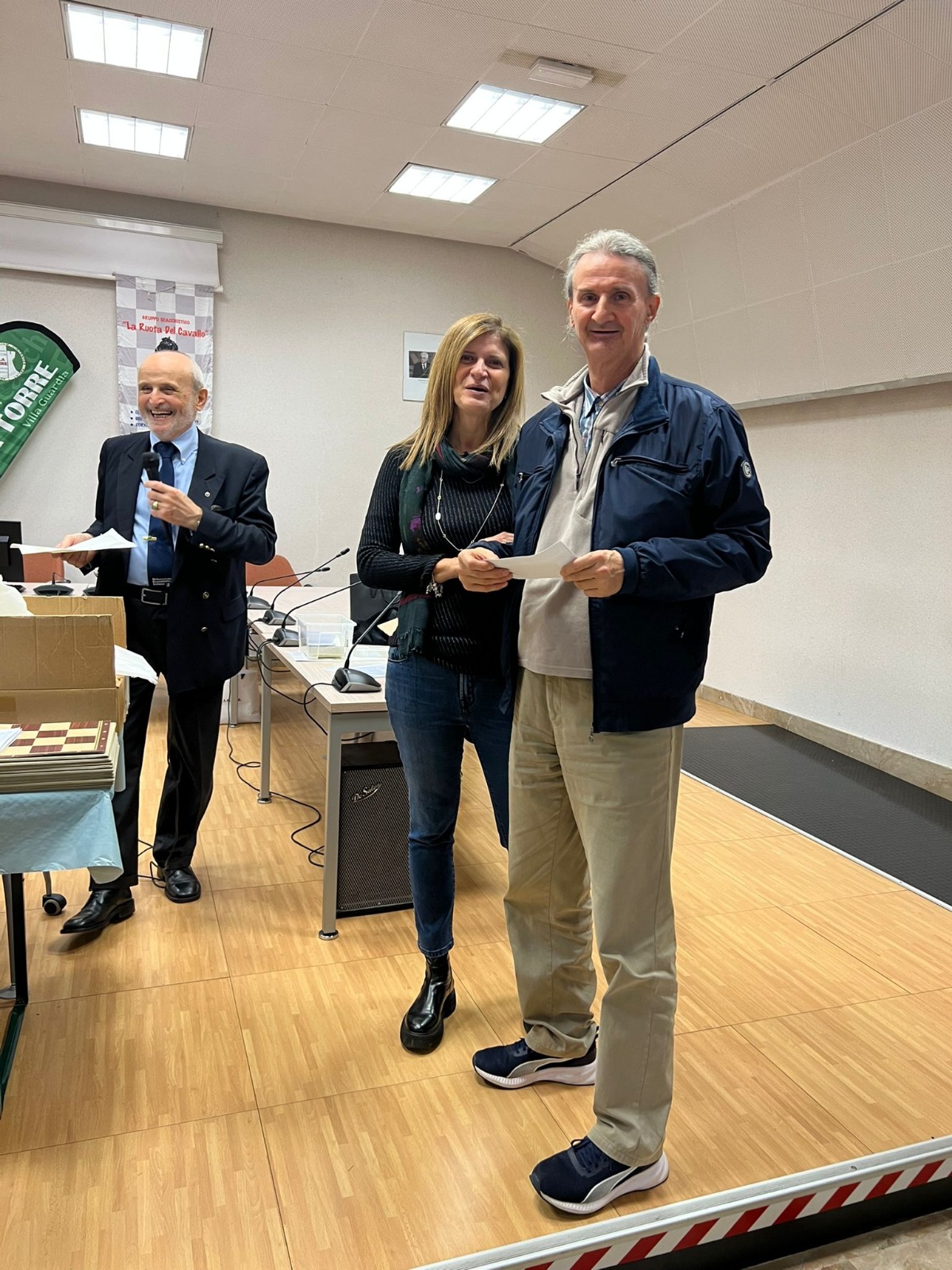 Un momento della premiazione durante i 'Campionati Provinciali Blitz e Rapid' a Rovellasca, con tre persone sul palco, inclusi due partecipanti che ricevono un premio.