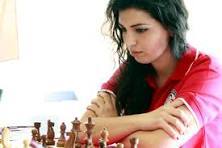 Giocatrice di scacchi concentrata durante una partita, con le braccia incrociate e scacchiere sul tavolo.
