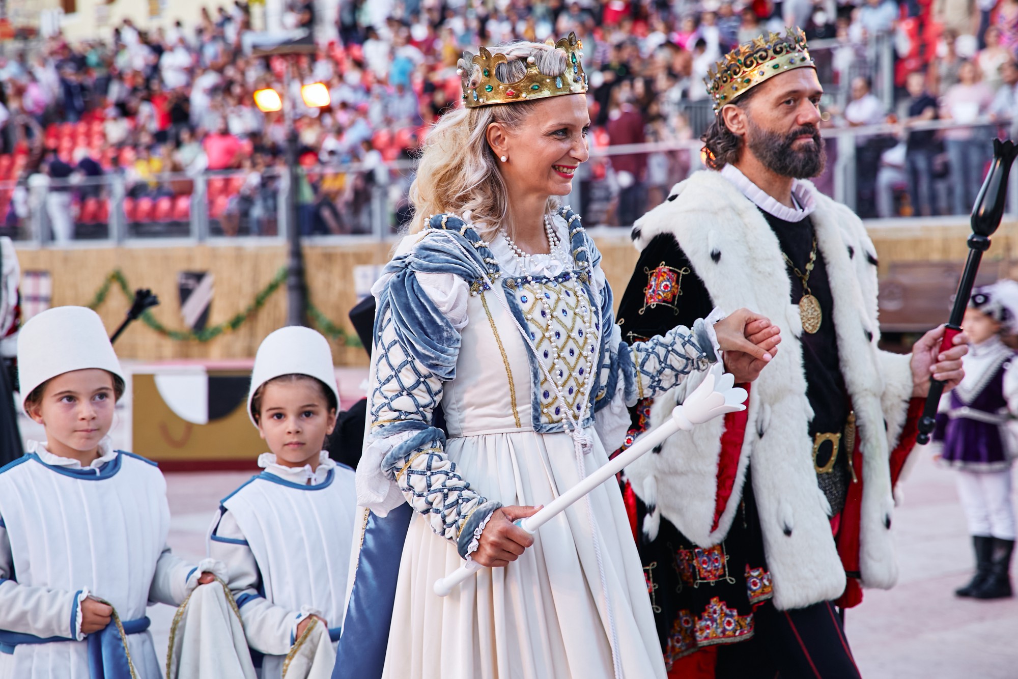 Una regina e un re in abiti regali, accompagnati da due bambini, durante una parata in un evento festivo.