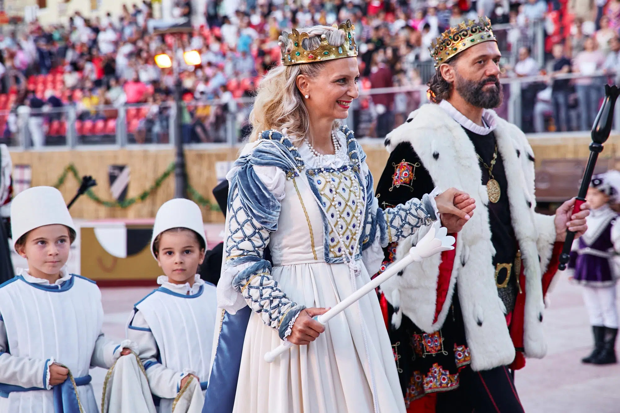 Una regina e un re in abiti regali, accompagnati da due bambini, durante una parata in un evento festivo.