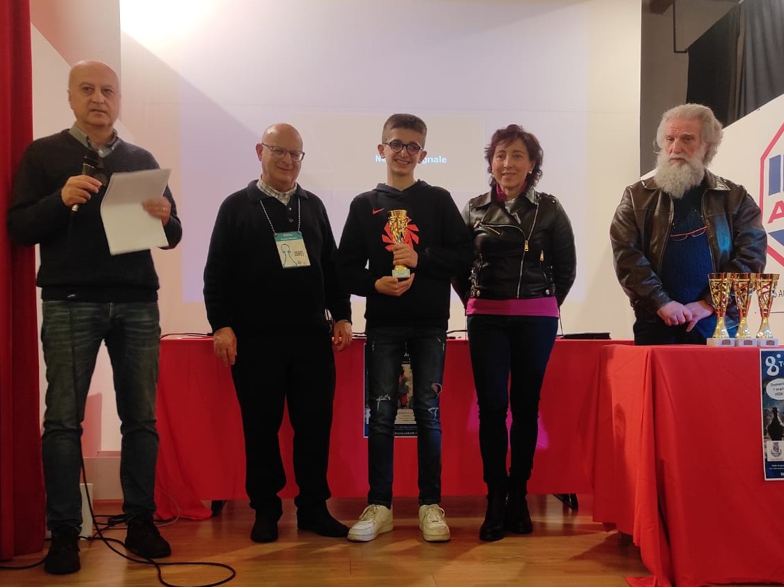 Cerimonia di premiazione con cinque persone, tra cui un giovane con un trofeo, in un ambiente festivo.
