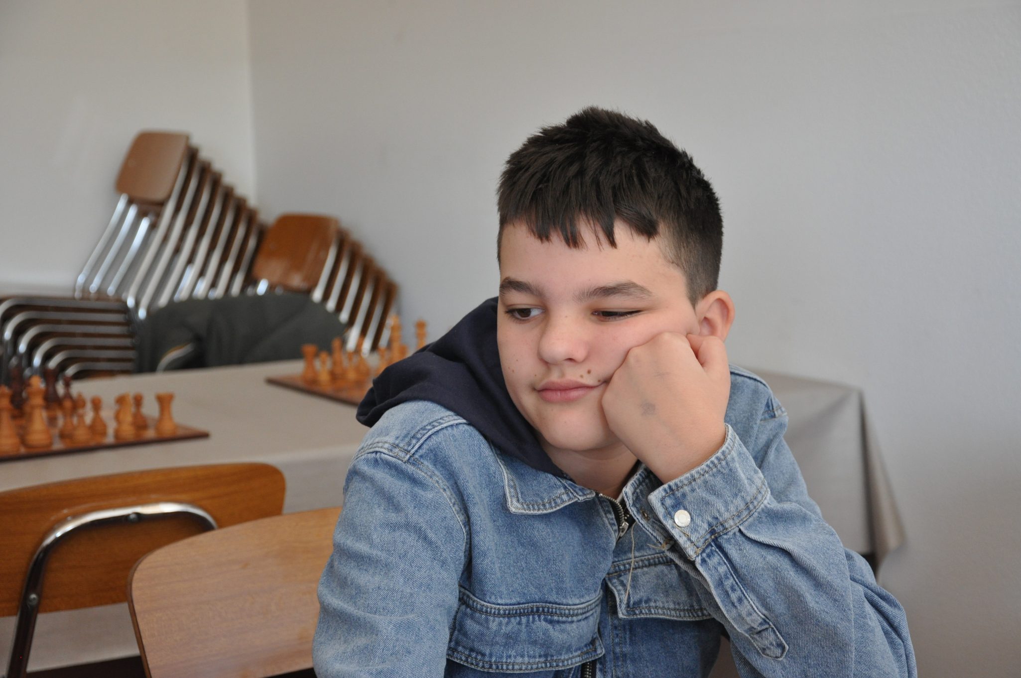 Ragazzo pensieroso seduto a un tavolo, con scacchi sullo sfondo.