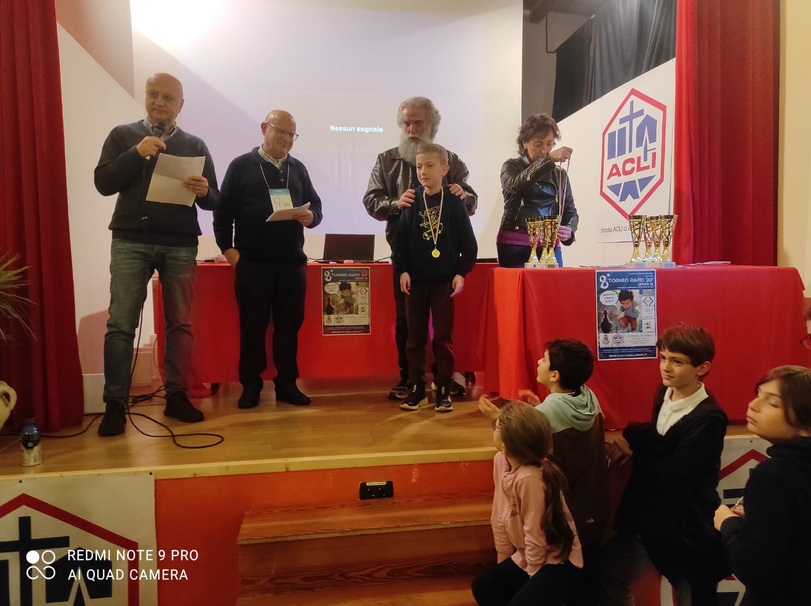 Un evento con adulti e bambini su un palco, con premi e riconoscimenti.