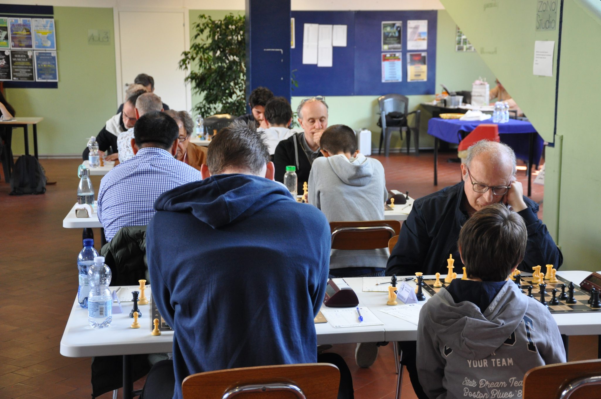 Una sala di torneo di scacchi con partecipanti seduti a tavoli, concentrati su partite di scacchi.