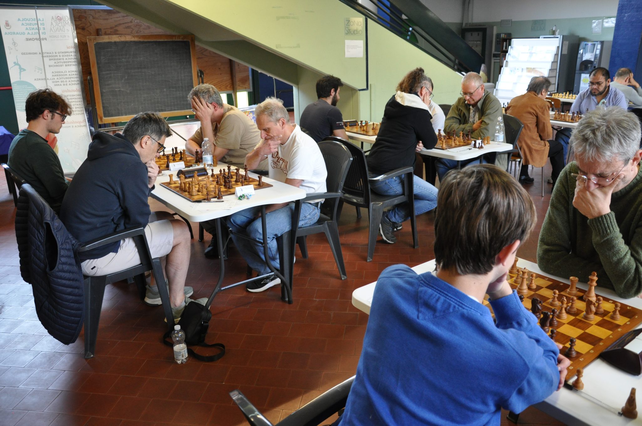 Un gruppo di persone che giocano a scacchi in una sala, ogni giocatore concentrato sulla propria partita.