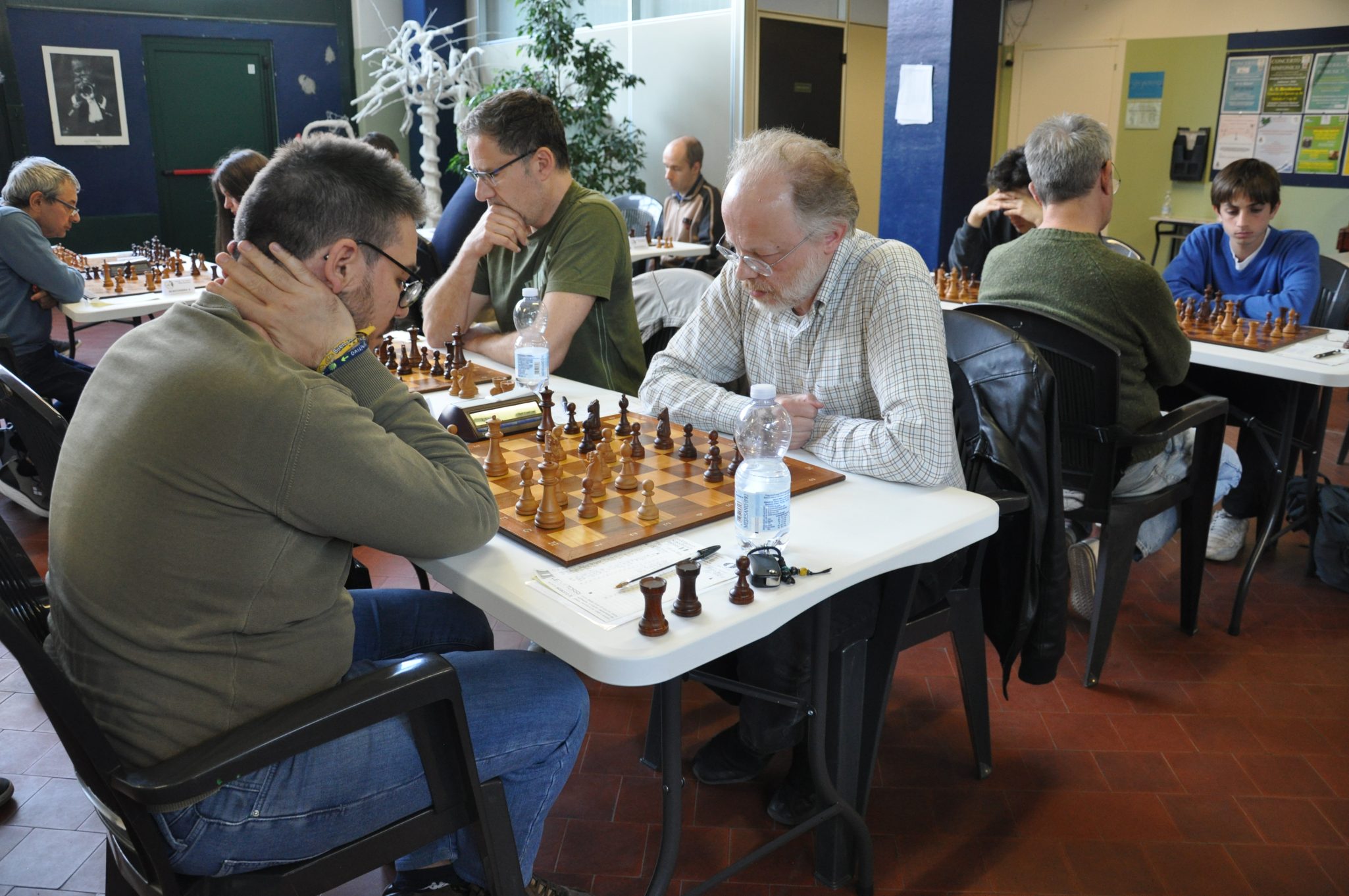 Giocatori di scacchi concentrati durante una partita in un torneo, seduti a tavoli con scacchiere e pezzi di legno.