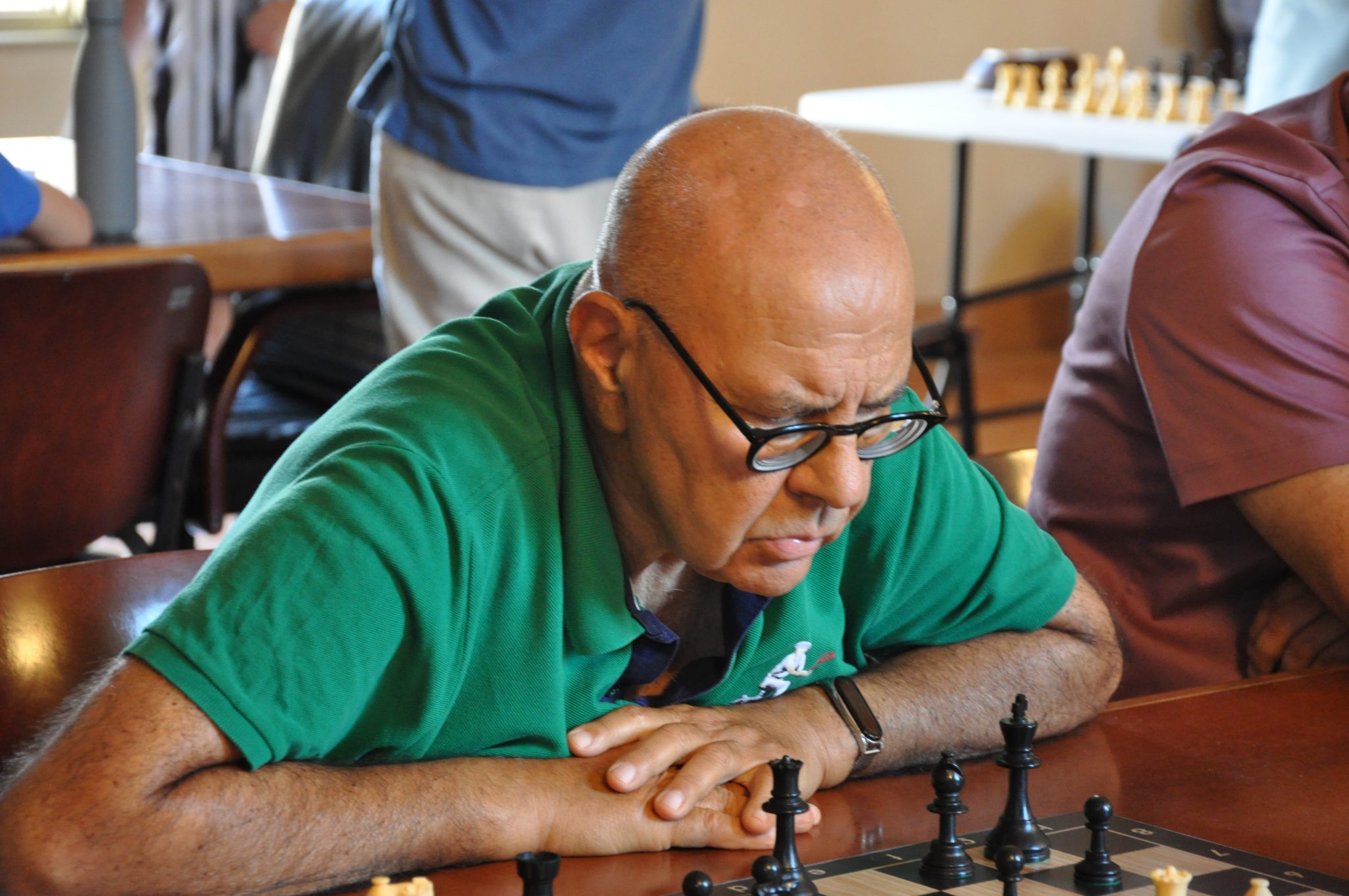 Giocatore di scacchi concentrato su una partita, con una maglietta verde, mentre osserva il tavolo da gioco.