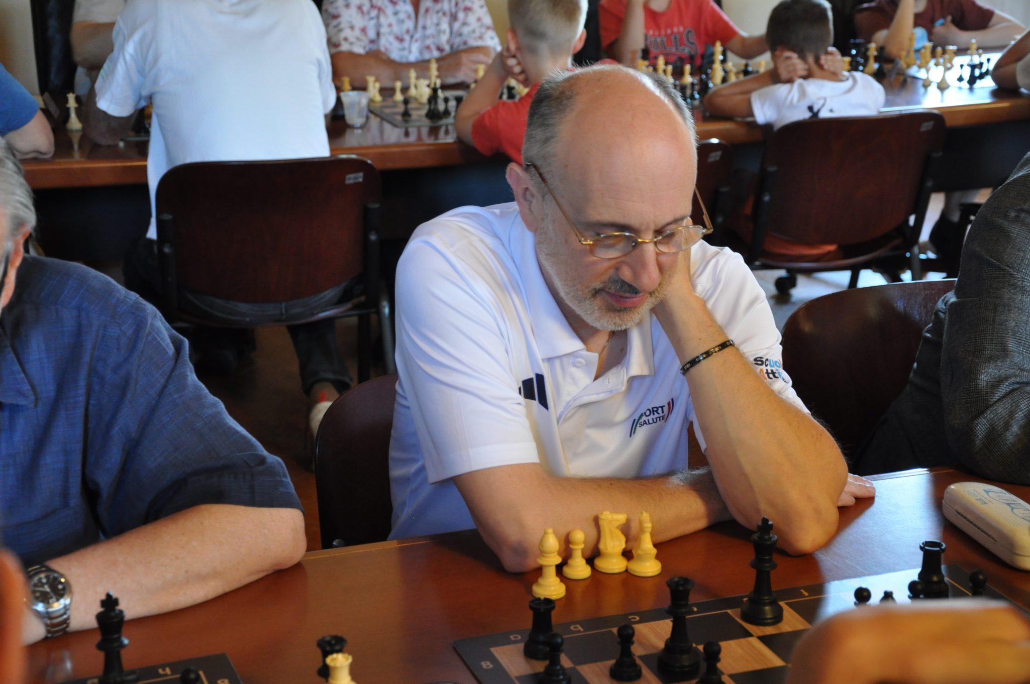 Un uomo che gioca a scacchi in un torneo, concentrato sul gioco. Si vedono pezzi di scacchi gialli e neri sulla scacchiera.
