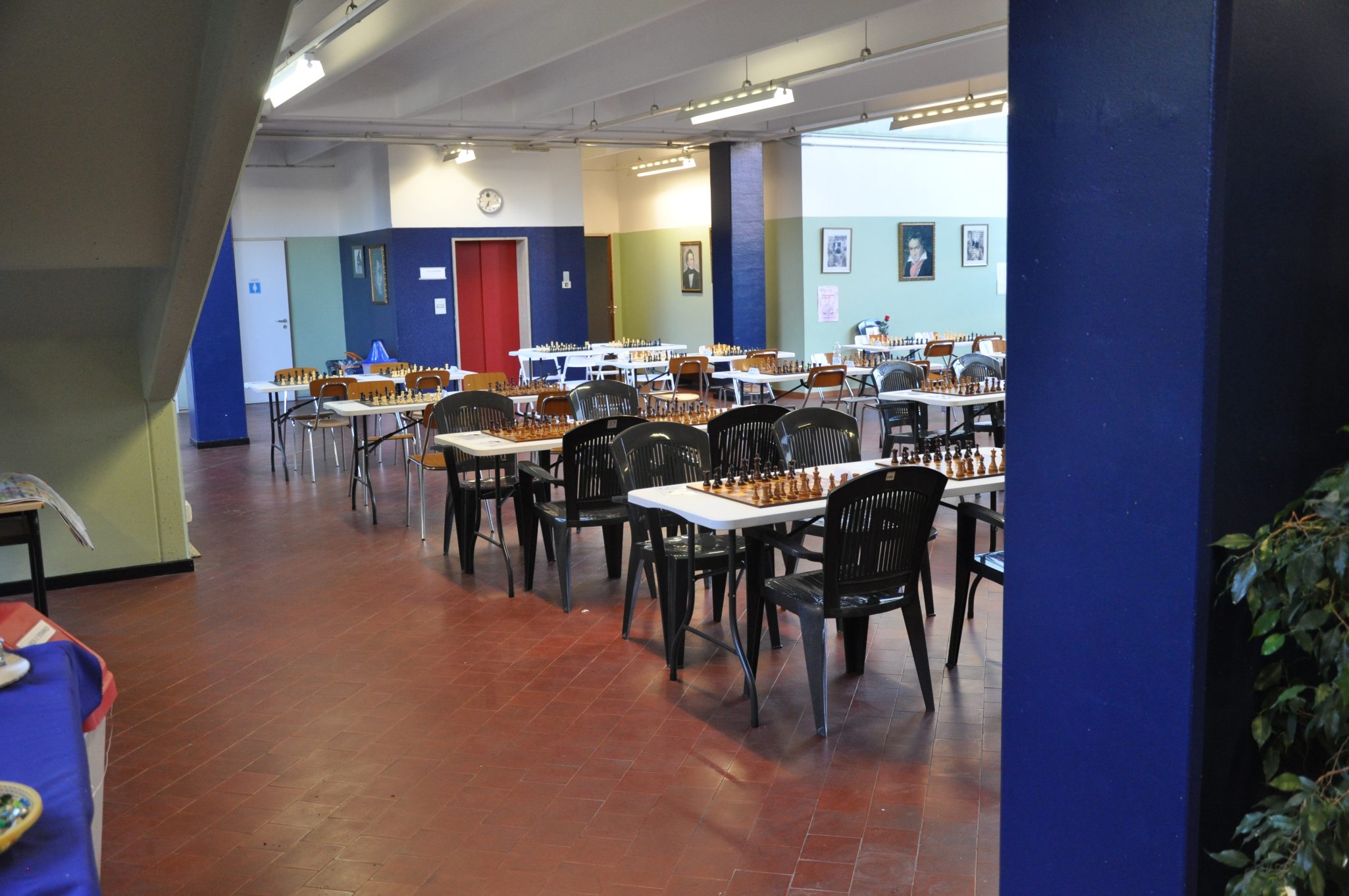 Interno di una sala con tavoli e sedie, arredato per il gioco degli scacchi. Alcuni tavoli hanno scacchiere pronte per essere usate.
