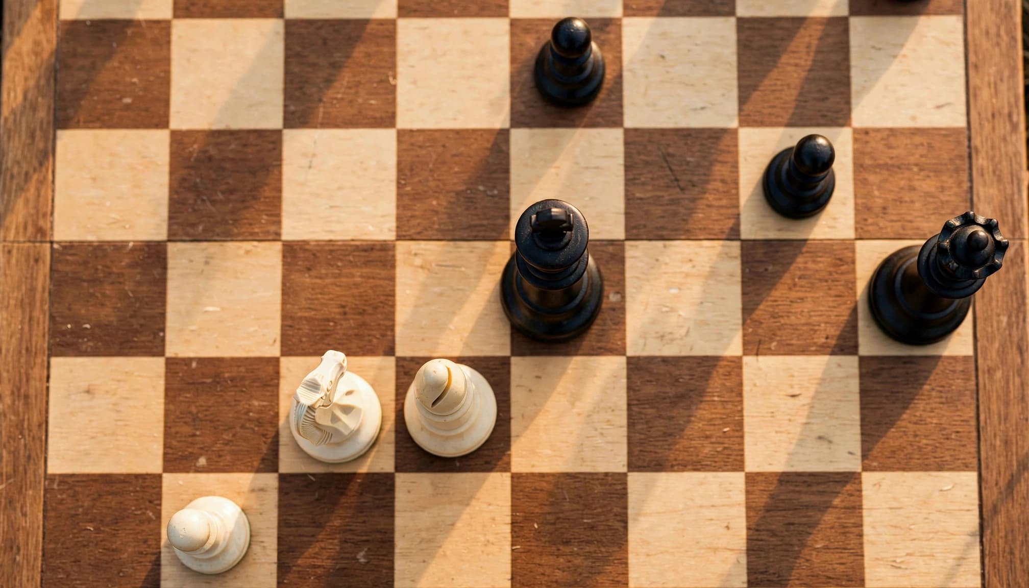 Scacchiera con pezzi bianchi e neri disposti su una superficie quadrata di legno.